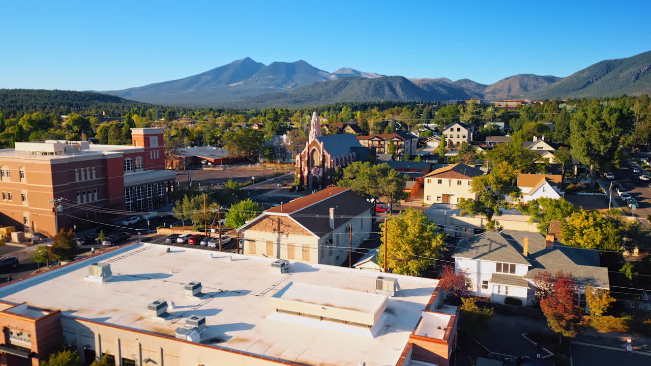 Approaching the iconic Gothic church of the Nativity in Flagstaff, Arizona, USA. Bright sun lights the cityscape. Drone footage. Verdant mountains at backdrop