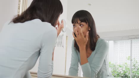 화장실에서 얼굴에 크림을 사용하고 거울을 보는 행복한 백인 여성