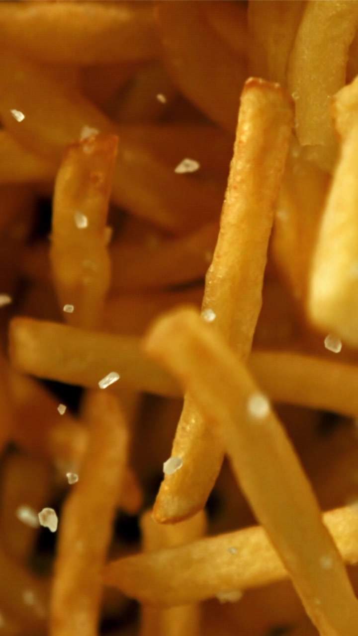 Close-up of Salt Crystals Falling onto Golden French Fries