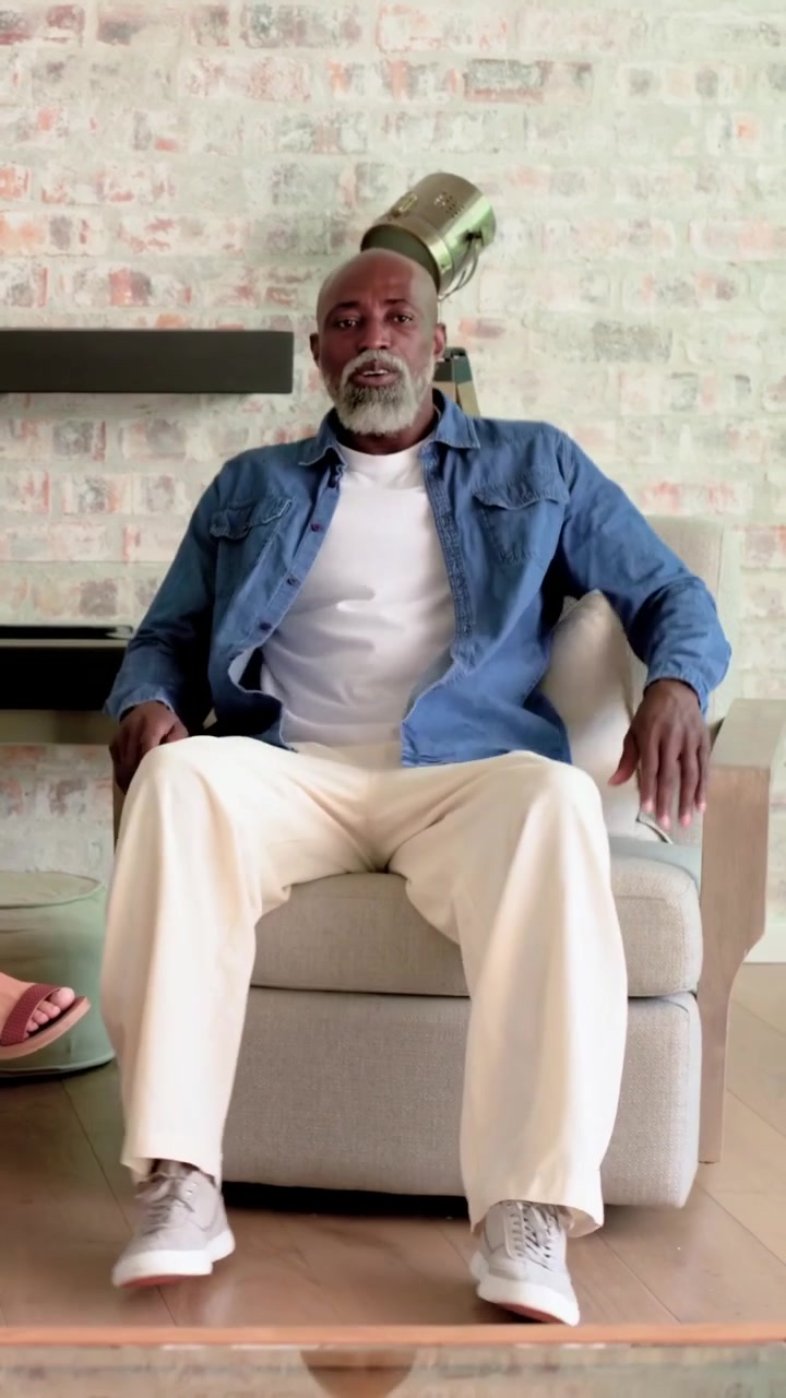Vertical video: Entering man in blue shirt crossing living room, joining seated woman on armchair