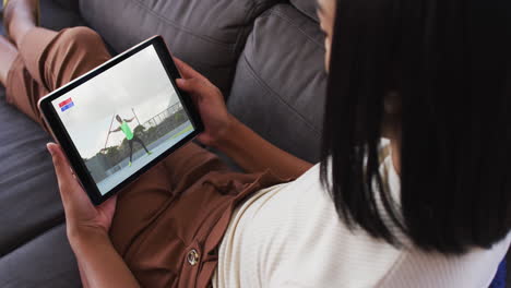 compuesto de una mujer sentada en casa en el sofá viendo un evento de jabalina de atletismo en una tableta
