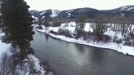 aerial - camera bends around tree revealing a beautiful snowy river