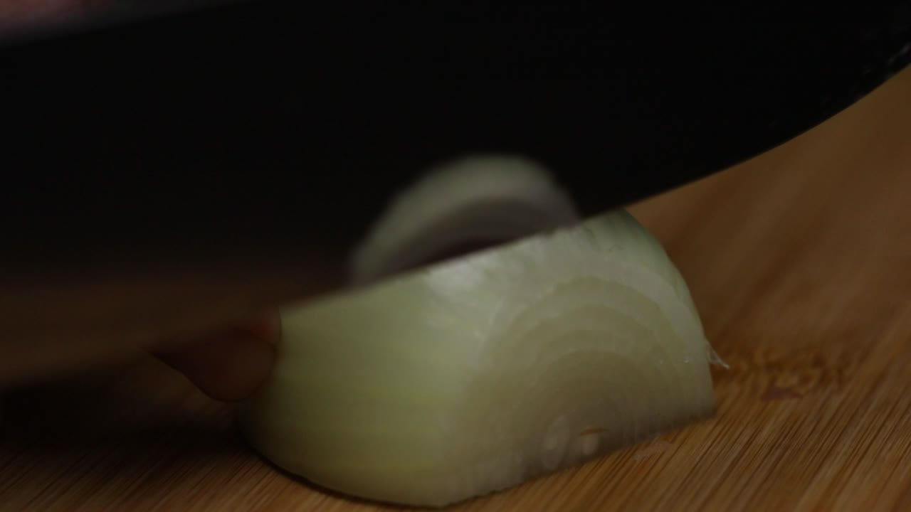 tiro de cerca en cámara lenta como cortar una cebolla en un escritorio de madera con un cuchillo grande y afilado