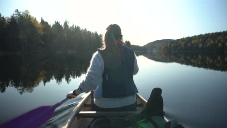 woman canoeing on beautiful lake in autumn, back view