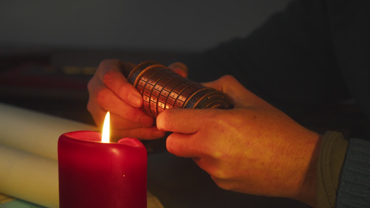 Close-up lilin menyala dengan tangan berbayang mengerjakan cryptex, menciptakan ketegangan dan kerahasiaan di lingkungan gelap yang sinematik.