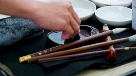 footage of a japanese man painting a nihonga, a traditional japanese painting, with brushes and black ink