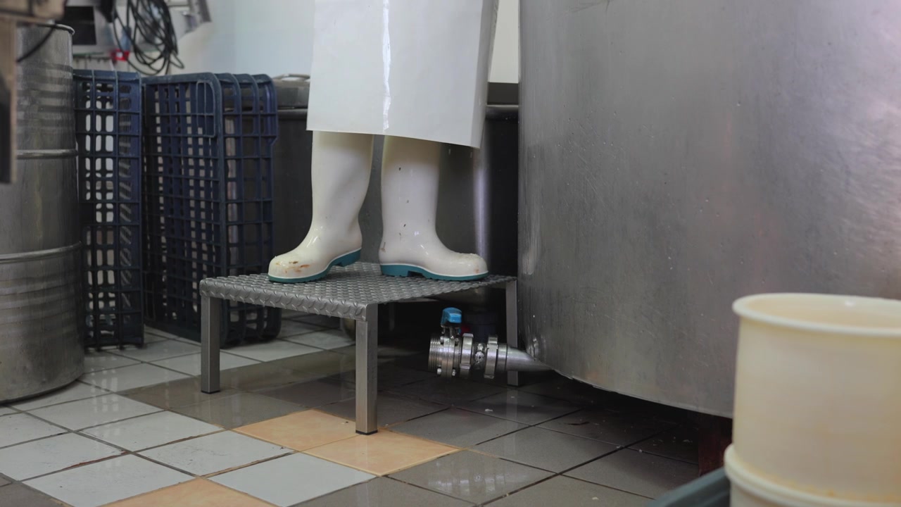 Cheesemaker working near a stainless steel tank during the dairy production process