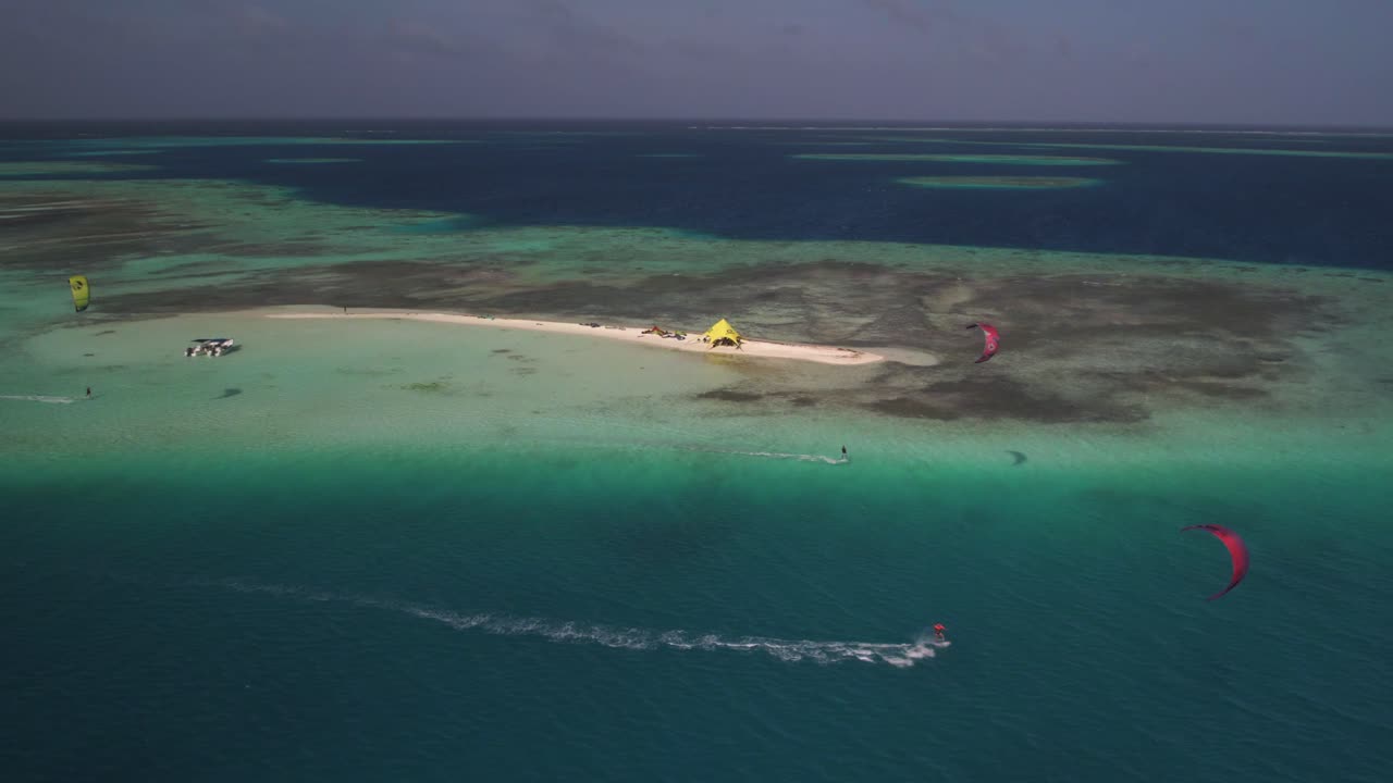 키트 서퍼 들 은 은 푸른 물 에 있는 작은 모래 섬 근처 에서 파도 를 타고