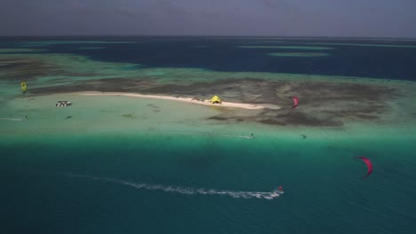 kitesurfers ride waves near a small sandy island in clear turquoise waters