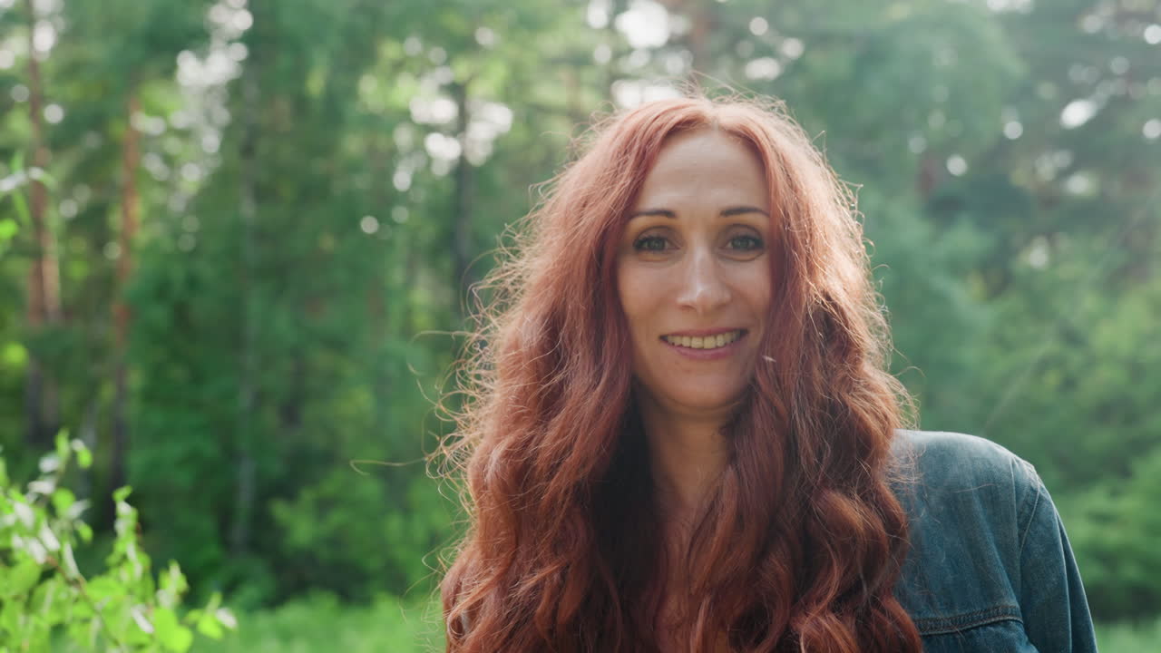 Portrait of family woman smiling gently in natural green forest, sunlight highlighting her face, peaceful outdoor atmosphere reflecting warmth, and maternal joy in bright summer day