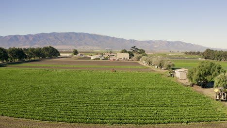 volando sobre tierras de cultivo e inclinándose hacia abajo sobre un granjero que trabaja en el campo de una granja del valle de salinas en ca