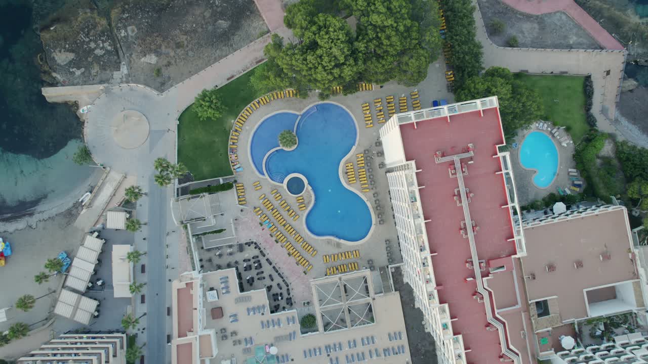 Descending from a top-down perspective, an aerial view captures the hotel facility and its outdoor swimming pool, close to the beach at a resort in Mallorca, Spain. Travel and holiday experiences.