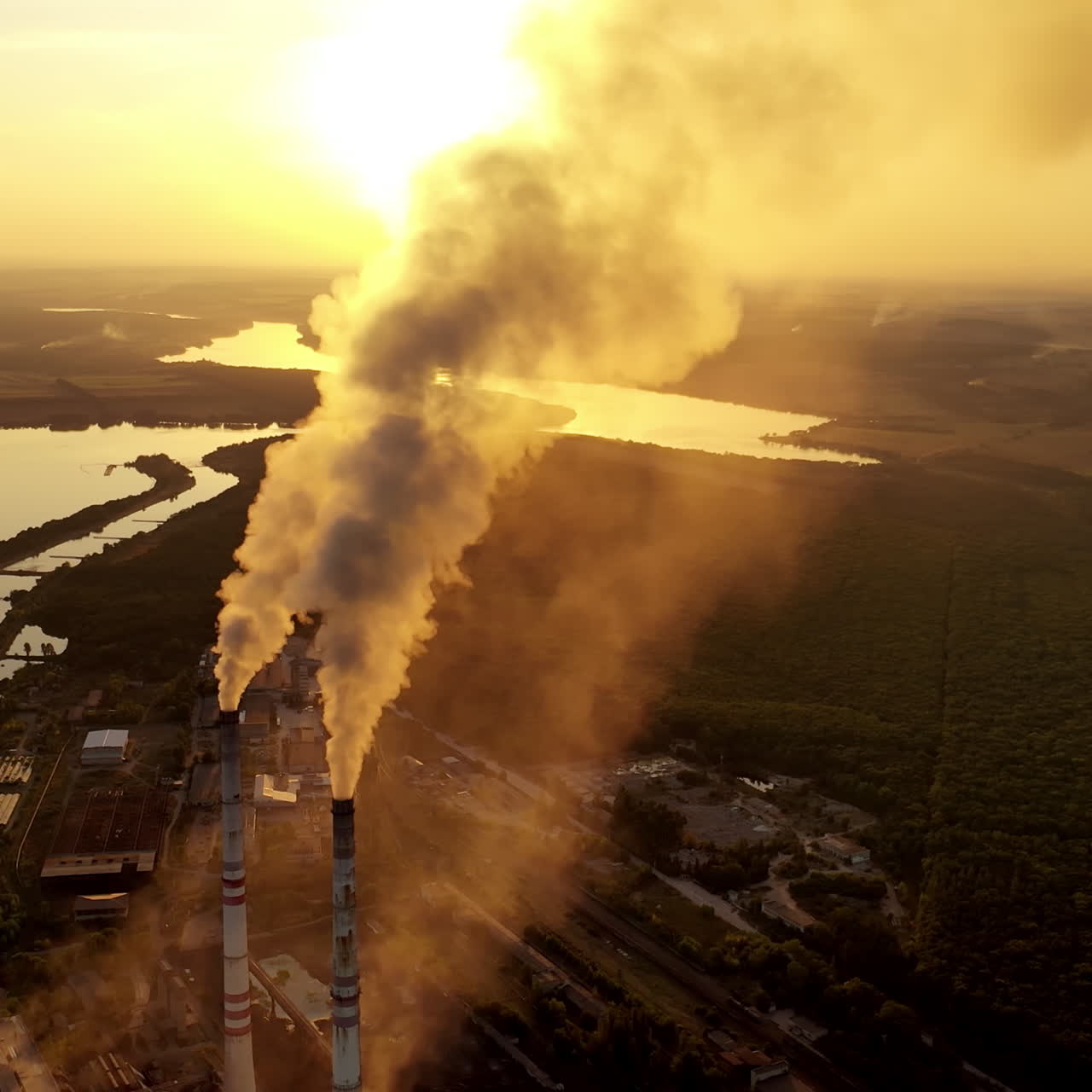 Industrial zone with pipes among nature. Thick white smoke is poured from the factory pipe at sunset. Pollution of the environment. Ecological problems. Aerial view