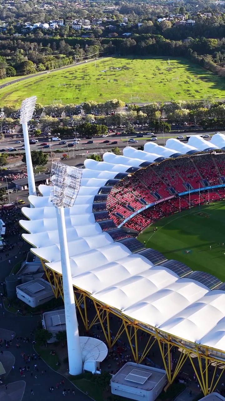 High-angle drone shot pans across a large stadium, parking lots, and green suburban fields.