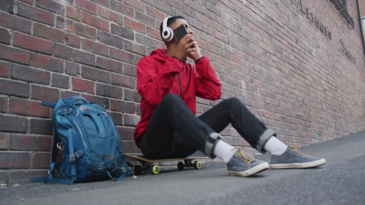 hombre de raza mixta sentado en una patineta y escuchando música en la calle
