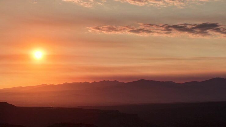Timelapse drone 4K UHD che cattura un cielo all'alba intenso e nebbioso. Il denso fumo degli incendi crea uno spesso strato atmosferico, oscurando il sole mattutino e le profonde valli del terreno montuoso e aspro sottostante.