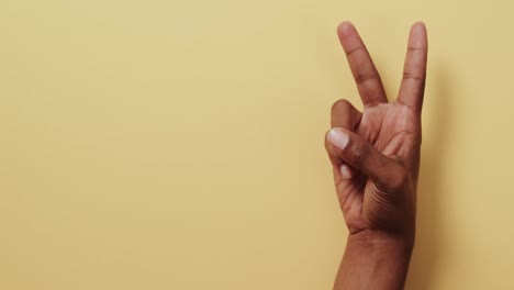 cerca de la mano de un hombre biracial mostrando un signo de paz con espacio de copia en fondo amarillo.