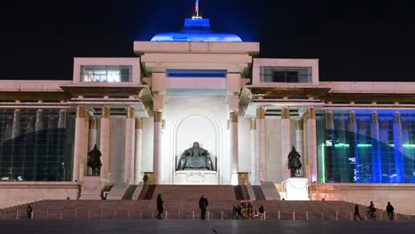 sukhbaatar square glows at night as people explore the area, featuring the bronze statue of genghis khan in front of the government palace and its flag in ulaanbaatar.