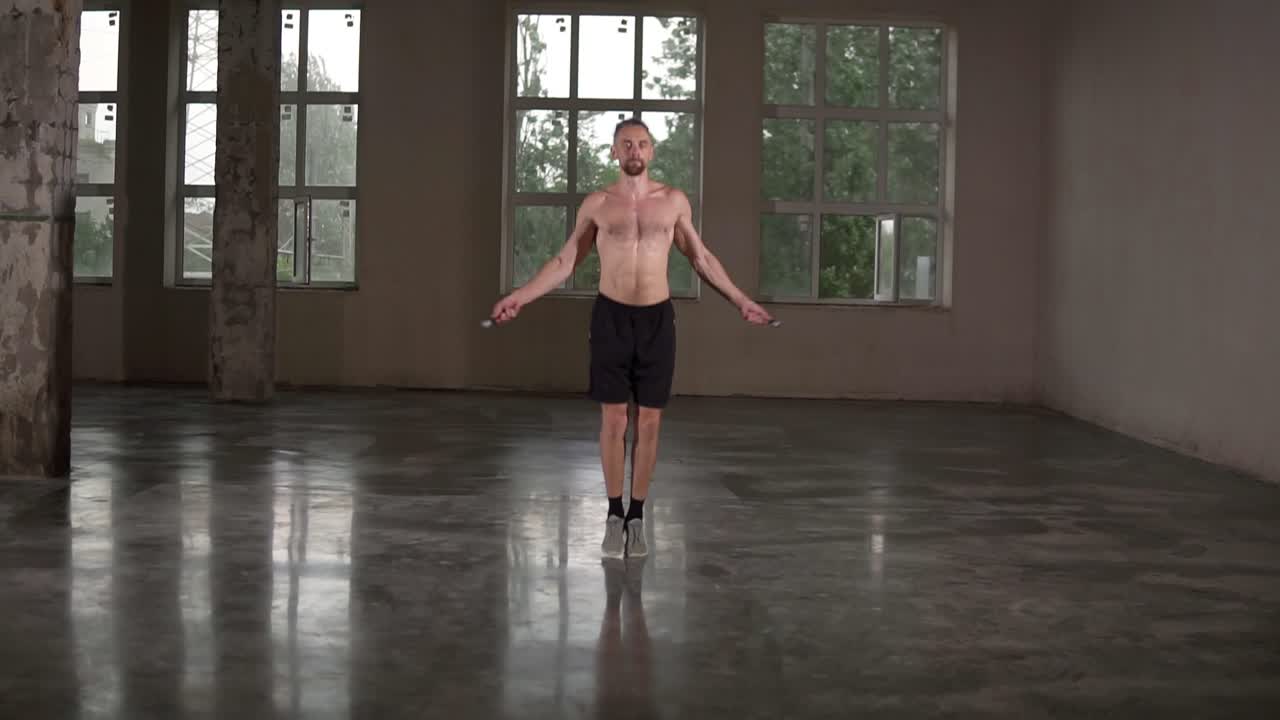 Fit shirtless sportsman is skipping with jump rope in gym studio concentrated on cardio exercise wearing black shorts. Workout, people and sports training concept
