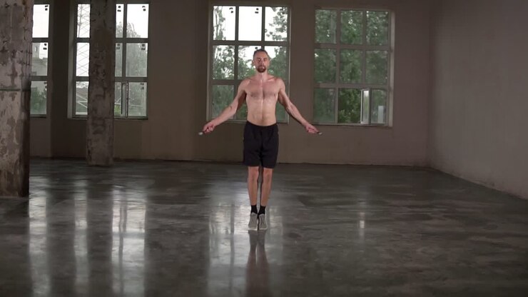 Fit shirtless sportsman is skipping with jump rope in gym studio concentrated on cardio exercise wearing black shorts. Workout, people and sports training concept
