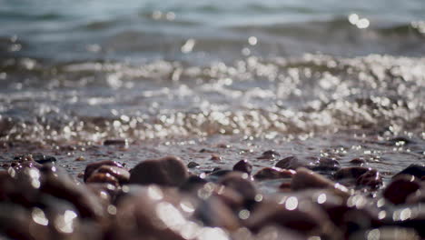 Waves-breaking-on-sunny-pebble-beach,-close-up-shot