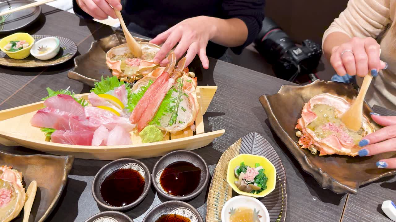 東京のレストランのテーブルで、新鮮な舟盛り刺身とカニ味噌を楽しむ客たち。