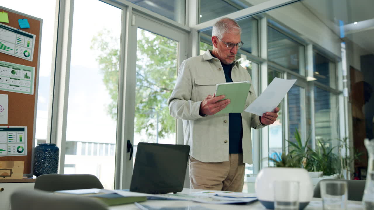 Senior Businessman Reviewing Documents and Tablet in Modern Office