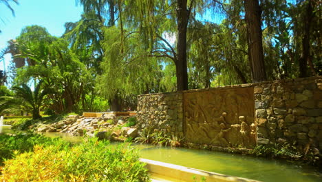 Tranquilo-Jardín-Con-Un-Muro-De-Piedra-Con-Un-Intrincado-Bajorrelieve,-Rodeado-De-Exuberante-Vegetación-Y-Un-Pequeño-Estanque-En-Málaga