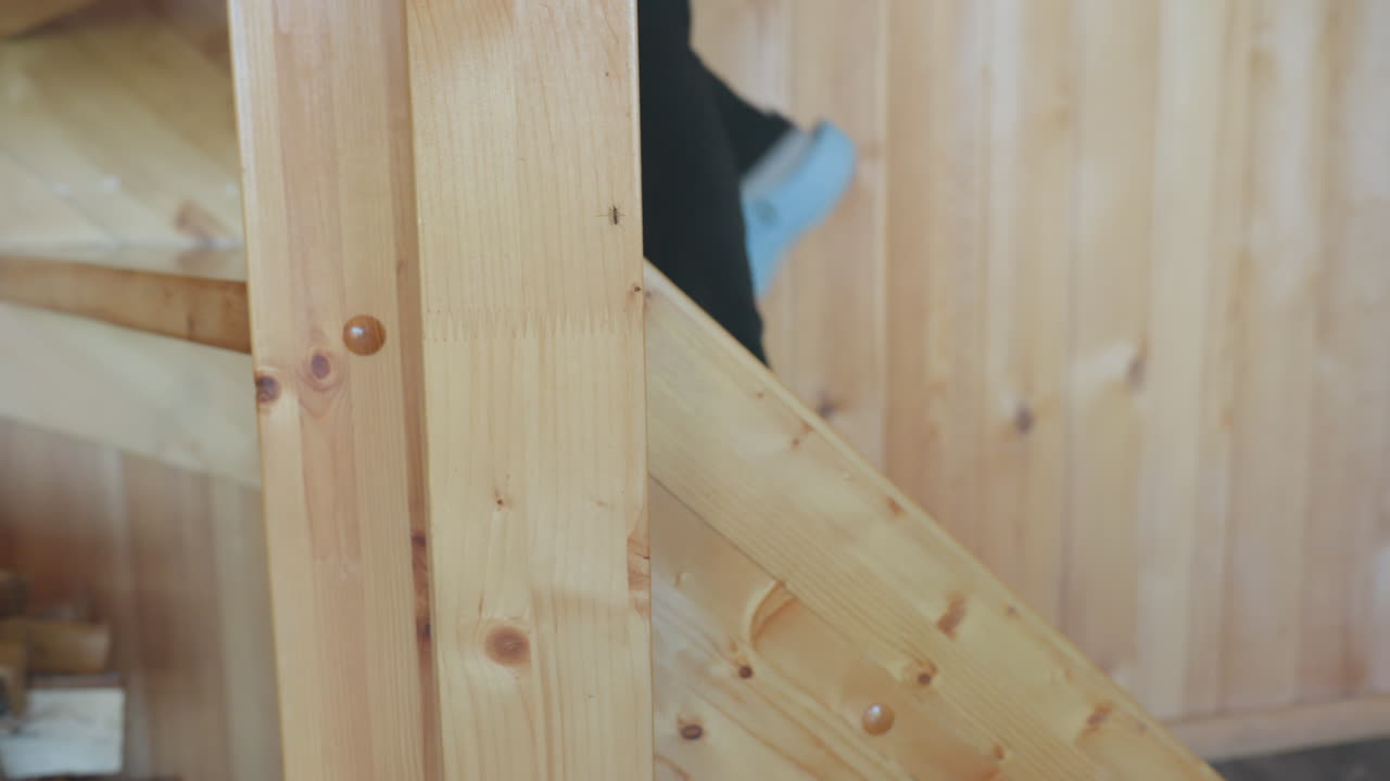 leg view of person in denim pants stepping up wooden staircase inside warm wooden cabin, focus on movement and natural textures, visible knee and foot suggest