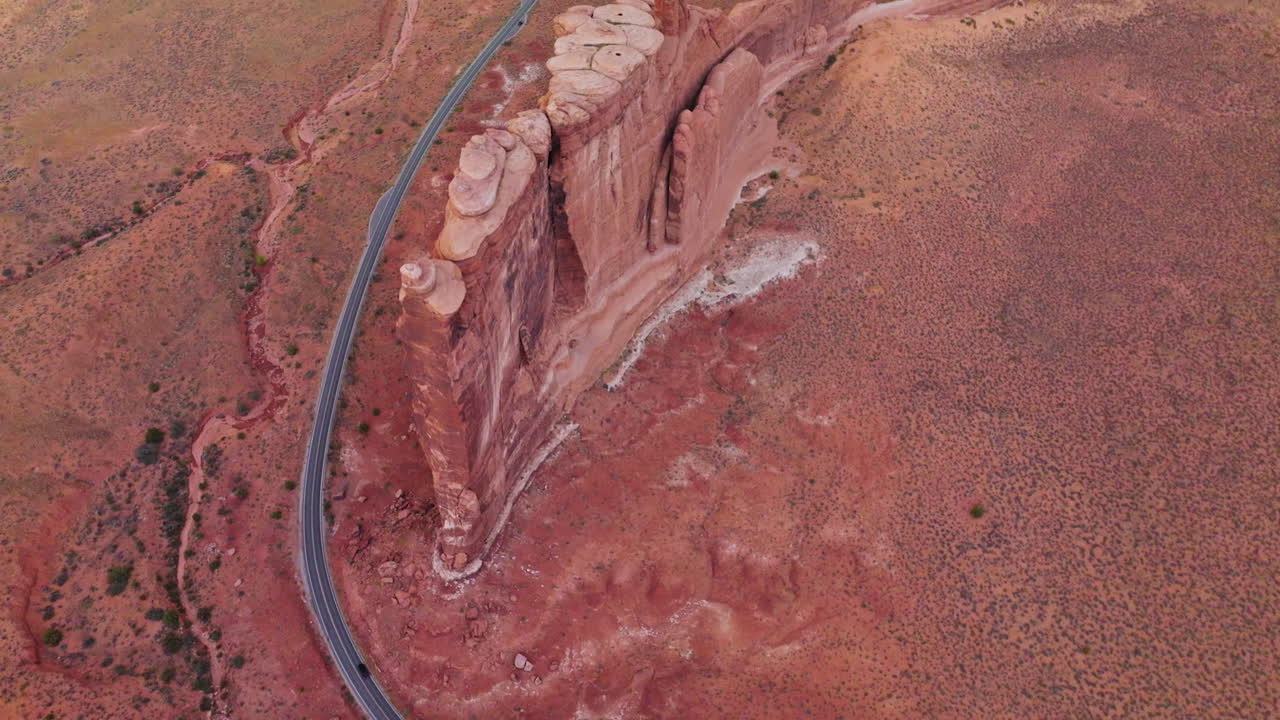 Stunning beautiful flat rock located in the middle of desert. Drone flight over the rounded peak mount and road passing below it. Top view.