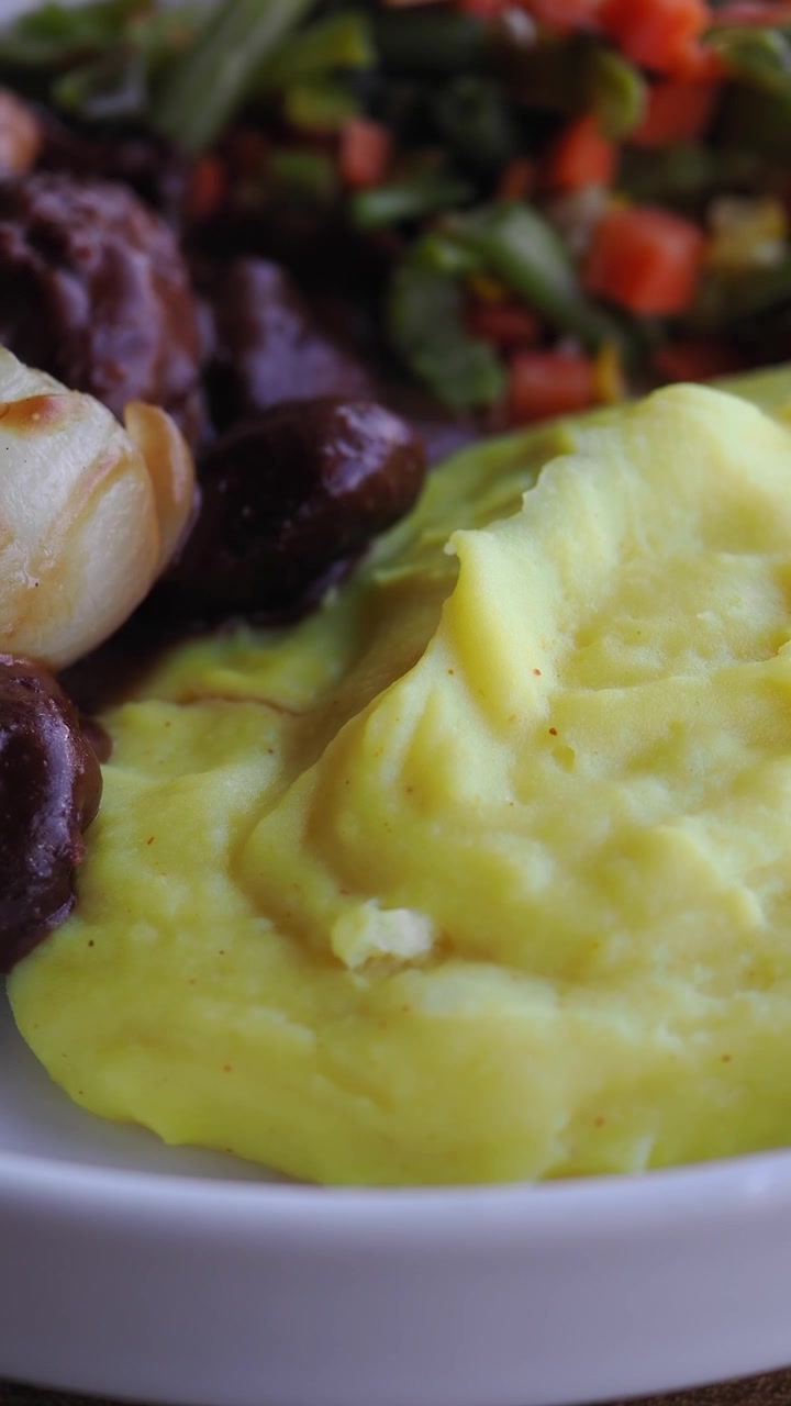 Primo piano di purè di patate cremoso servito con verdure e carne.