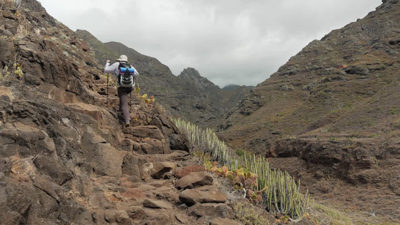 una mujer excursionista en un camino rocoso empinado en las montañas de anaga en tenerife, españa con enormes montañas en el fondo