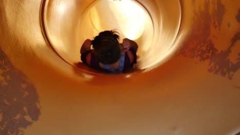 Little-girl-in-overalls-throws-up-peace-signs-before-sliding-down-yellow-tube-slide