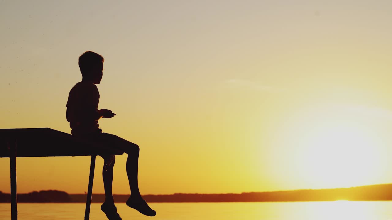 child is sitting on the end of the masonry and throwing pebbles into the water at sunset