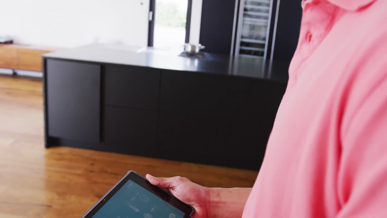 Video of happy biracial man checking weather on tablet, smiling and looking around in holiday home