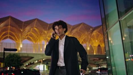 Young-man-talking-phone-at-illuminated-city.-Smiling-businessman-waving-arm