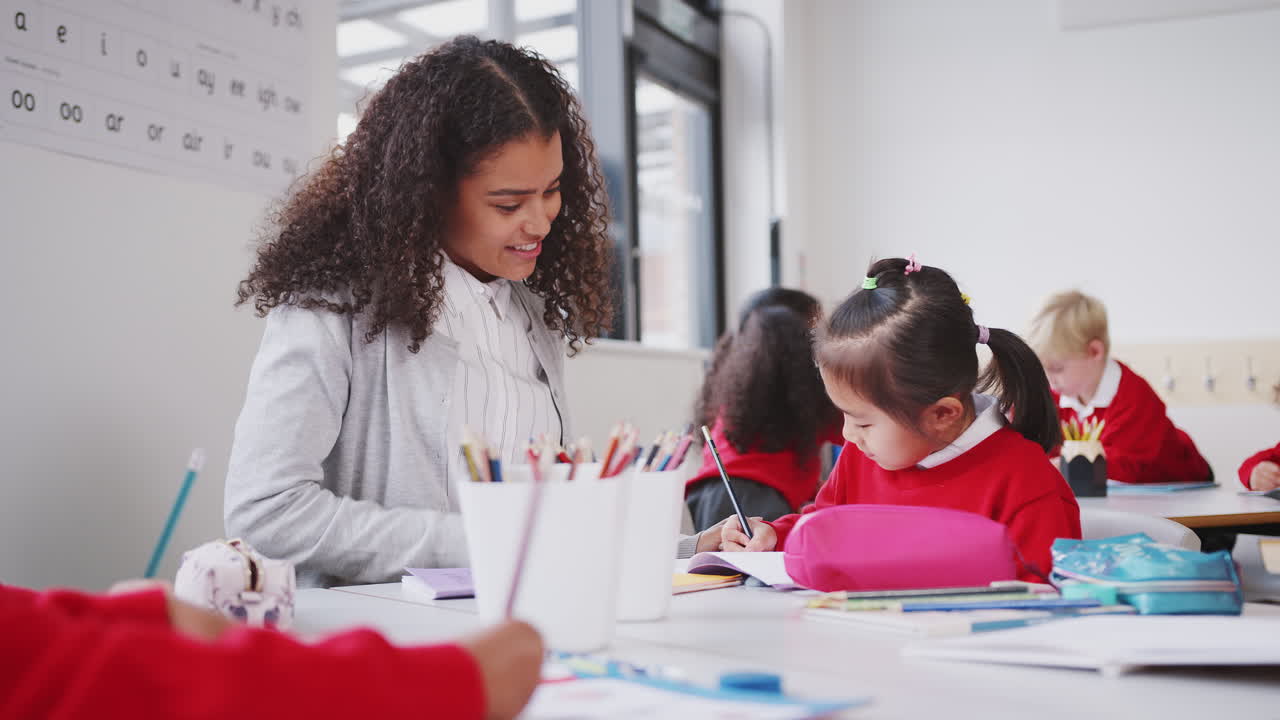 maestra y escolar china sentadas en la mesa en la clase de la escuela infantil, de cerca, ángulo bajo