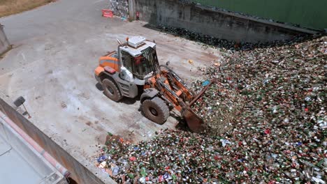 la excavadora de carretilla está agarrando vidrio, la máquina de servicio pesado tiene un brazo largo equipado con un accesorio para agarrar vidrio, vista aérea de drones, concepto de reciclaje de vidrio
