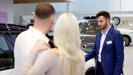 footage from the back - couple talking to car dealer in dealership discussing the chosen car