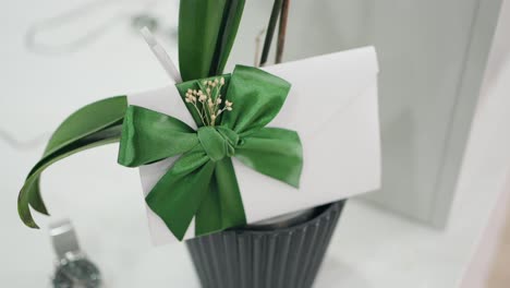 white envelope wrapped with a green satin bow and small flowers placed on a plant