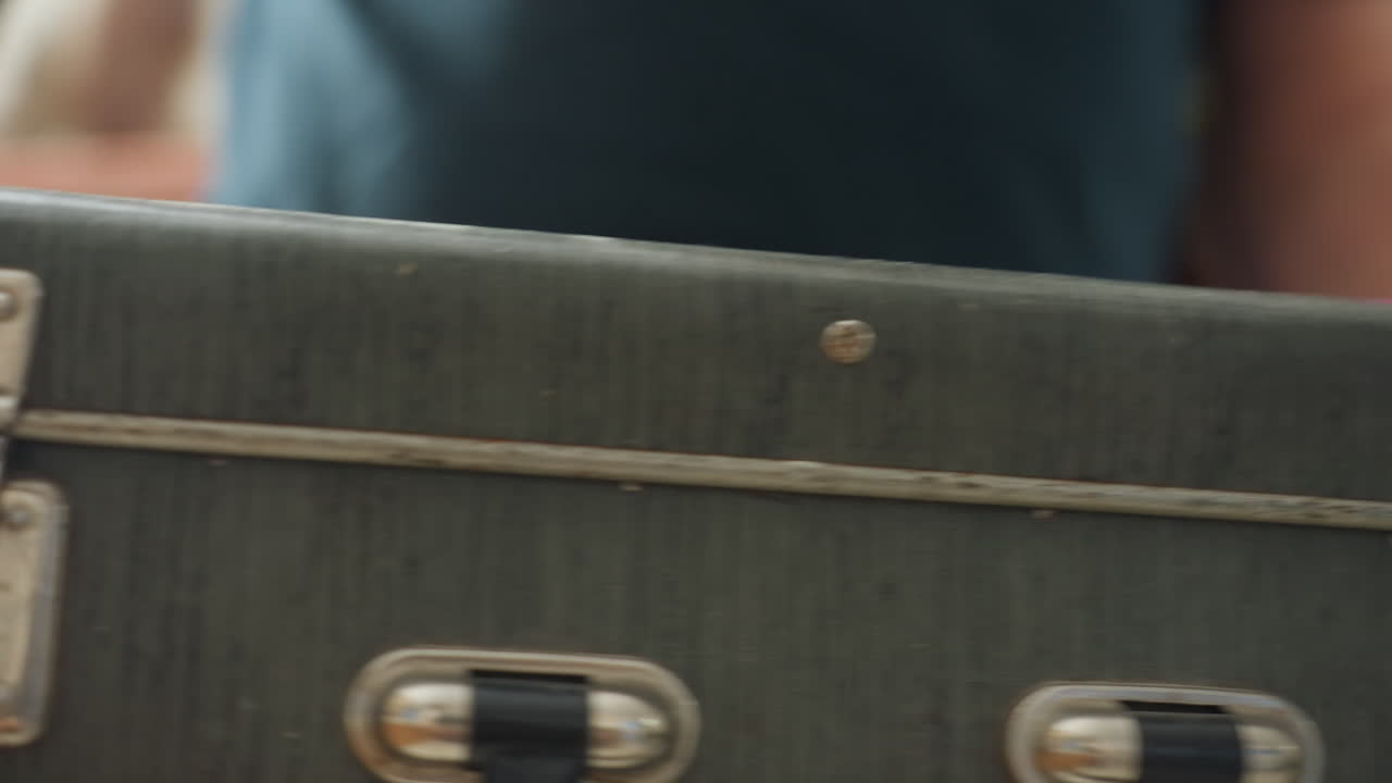 Close-up of man holding vintage box with metal corners and handle, showing details of box lock and craftsmanship in casual setting, likely preparing for a family activity or celebration