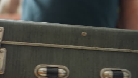 close-up of man holding vintage box with metal corners and handle, showing details of box lock and craftsmanship in casual setting, likely preparing for a family activity or celebration