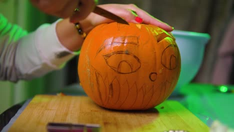 mujer con uñas rojas tallando cejas en la calabaza con fondo colorido