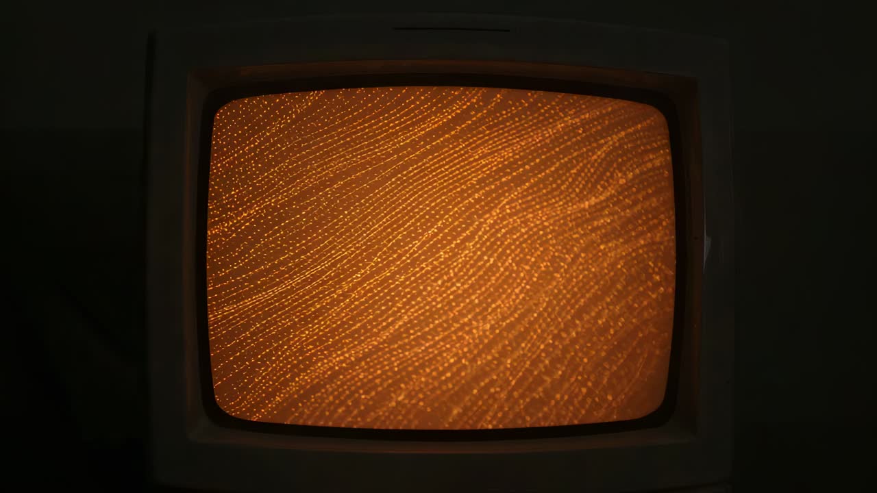 Loş ışıklı bir odada dalgalanan turuncu noktalı dalgaları gösteren CRT TV, kablosu görülebilir