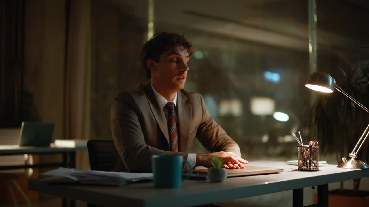 Primo piano di un lavoratore notturno che sfoglia documenti alla luce della lampada da ufficio. Uomo che chiude il computer