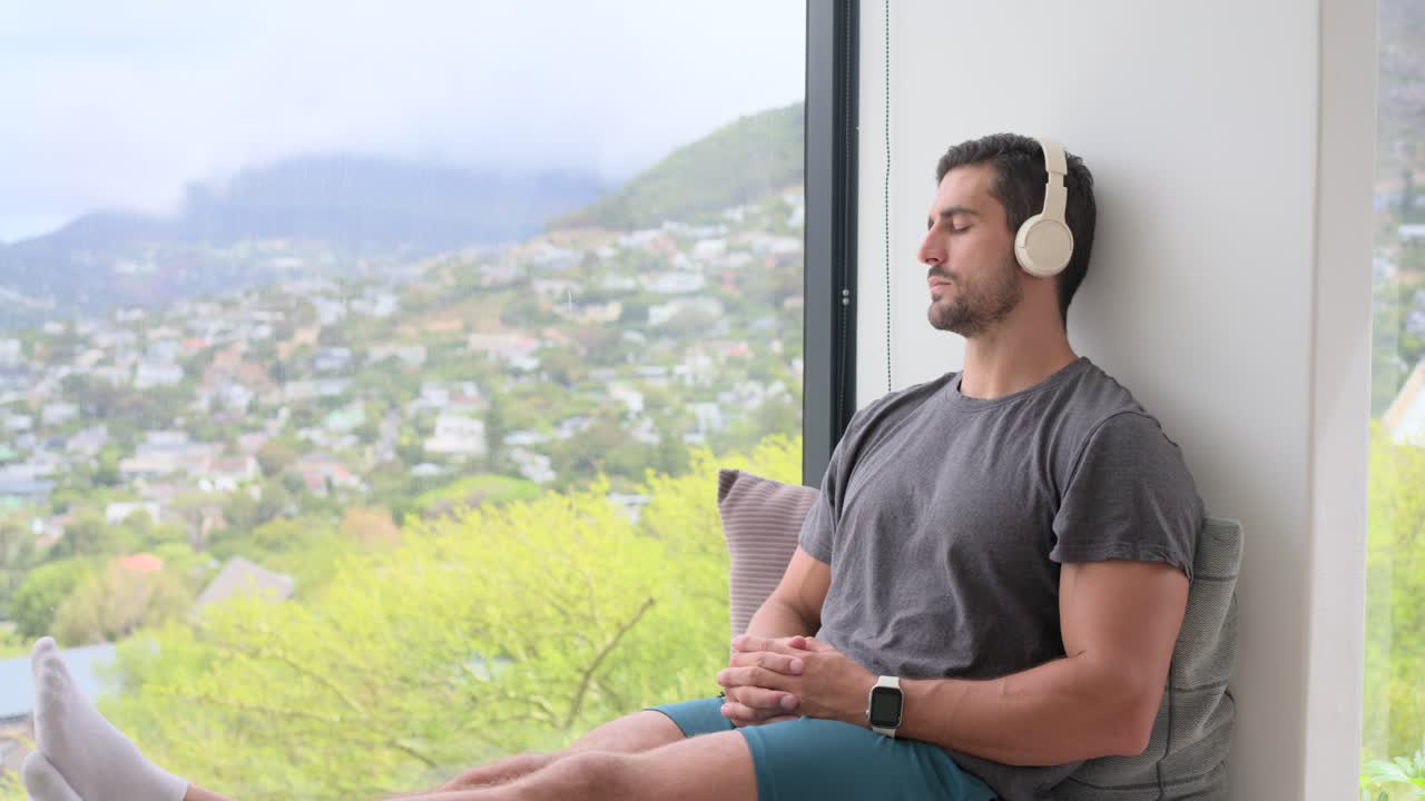 Uomo adulto che indossa le cuffie, usa il telefono, selezionando l'audio, rilassandosi sul sedile accanto alla finestra, spazio per il testo.