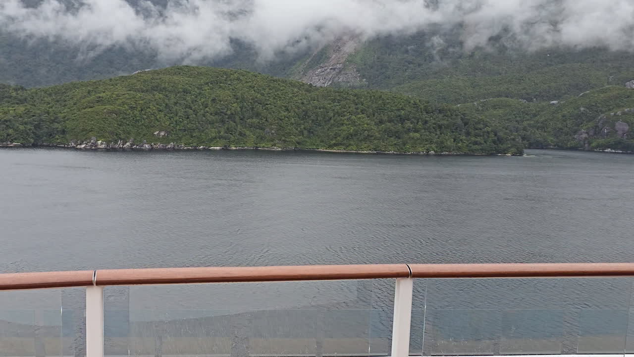 Milford Sound fiord landscape showcasing green forested mountains, deep water, and moody sky with low hanging clouds on an overcast day in the South Island of New Zealand