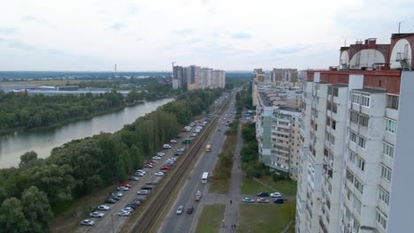 Vista-Aérea-Del-Tráfico-En-La-Calle-Mykoly-Zakrevskoho,-Un-Río-Y-Edificios-De-Apartamentos-Antiguos,-En-El-Barrio-De-Troieshchyna,-Día-Nublado,-En-La-Ciudad-De-Kiev,-Ucrania---Aumento,-Disparo-De-Drones