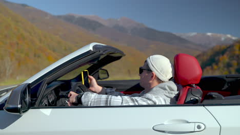 hombre conduciendo un coche descapotable a través de montañas pintorescas en otoño