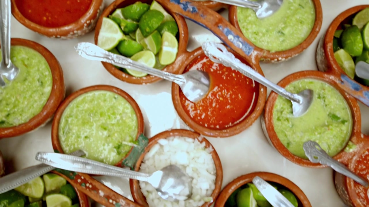 Vista superior de salsas mexicanas tradicionales, cebolla picada y gajos de lima servidos en cuencos de cerámica rústicos durante la preparación de la comida